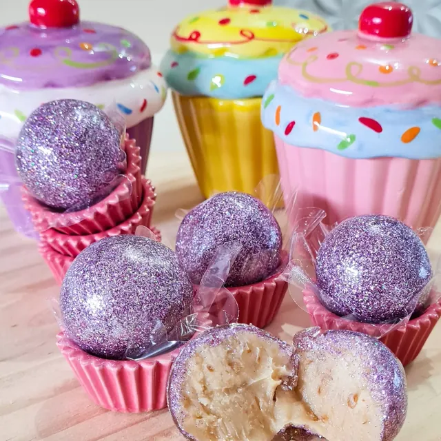 Balas caramelizadas com purpurina comestível, em forminhas rosa ao lado de cupcakes decorativos